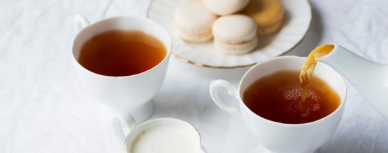 Two white cups filled with coffee and a white plate with cream biscuits